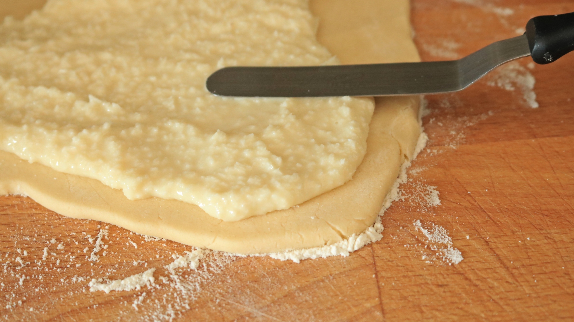 A spatula spreading topping onto a cookie dough sheet.