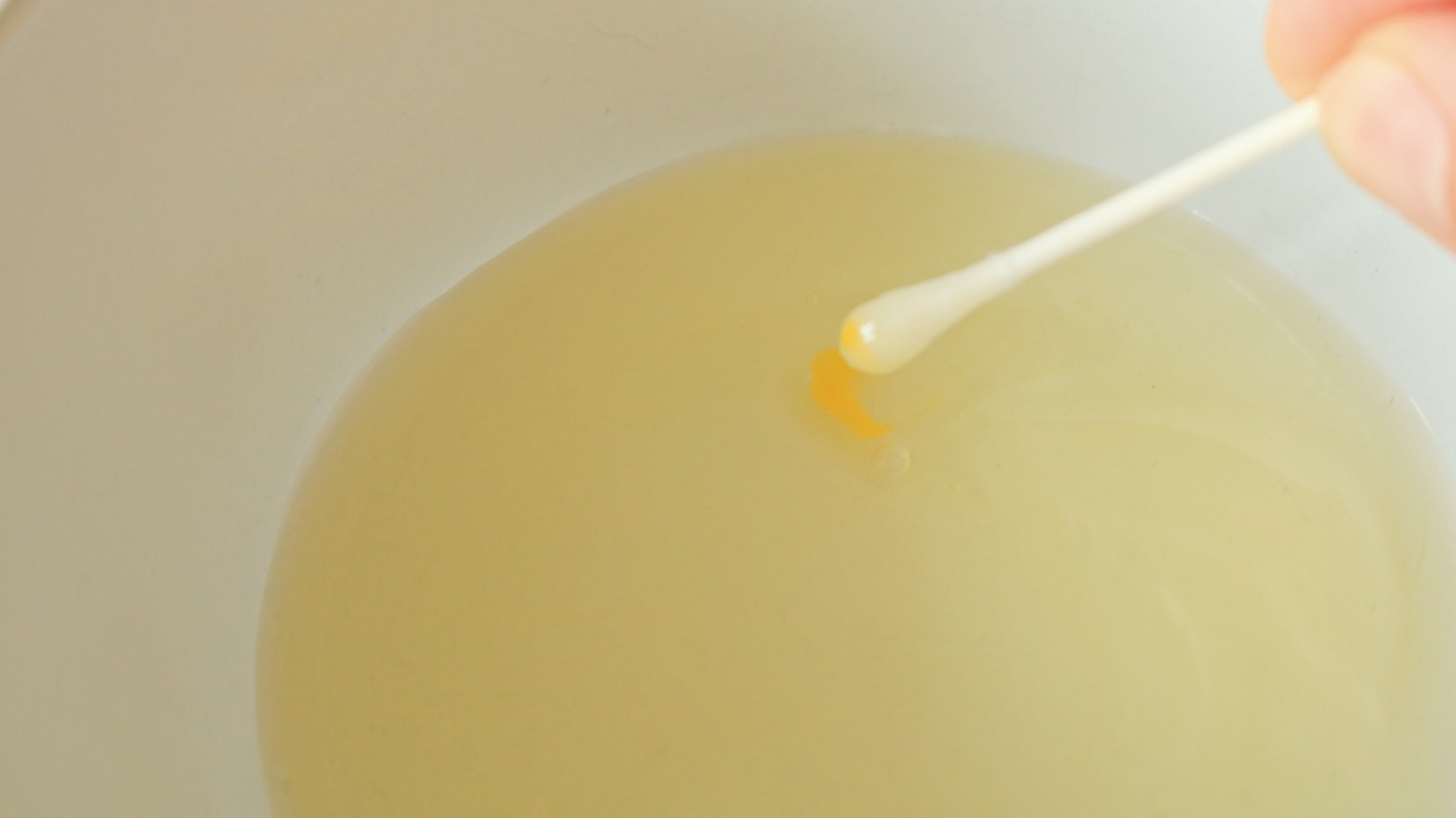 A cotton swab fishing out streaks of yolk from a bowl of whites.