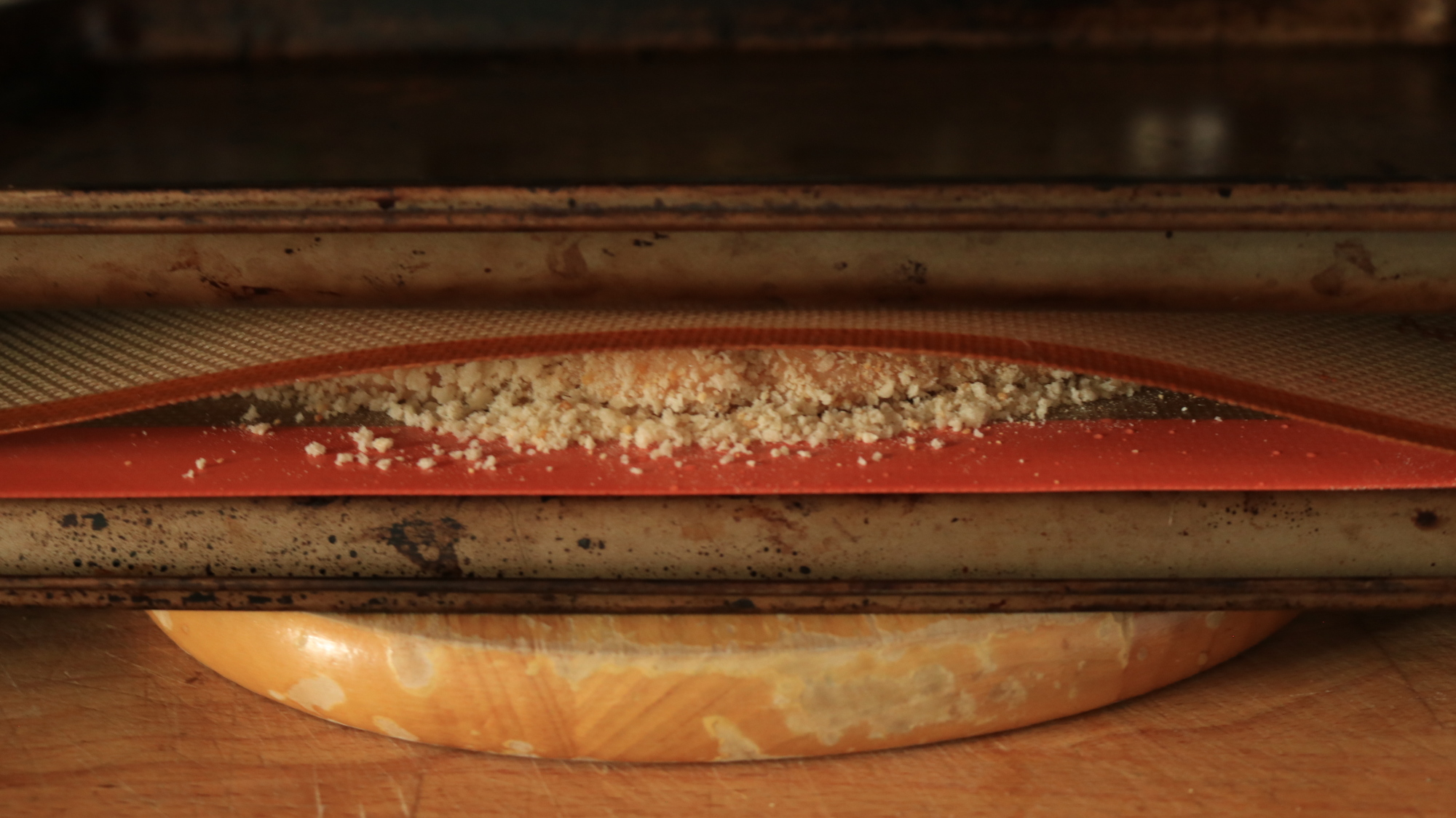 Two sheet trays sandwiching a breaded chicken patty.