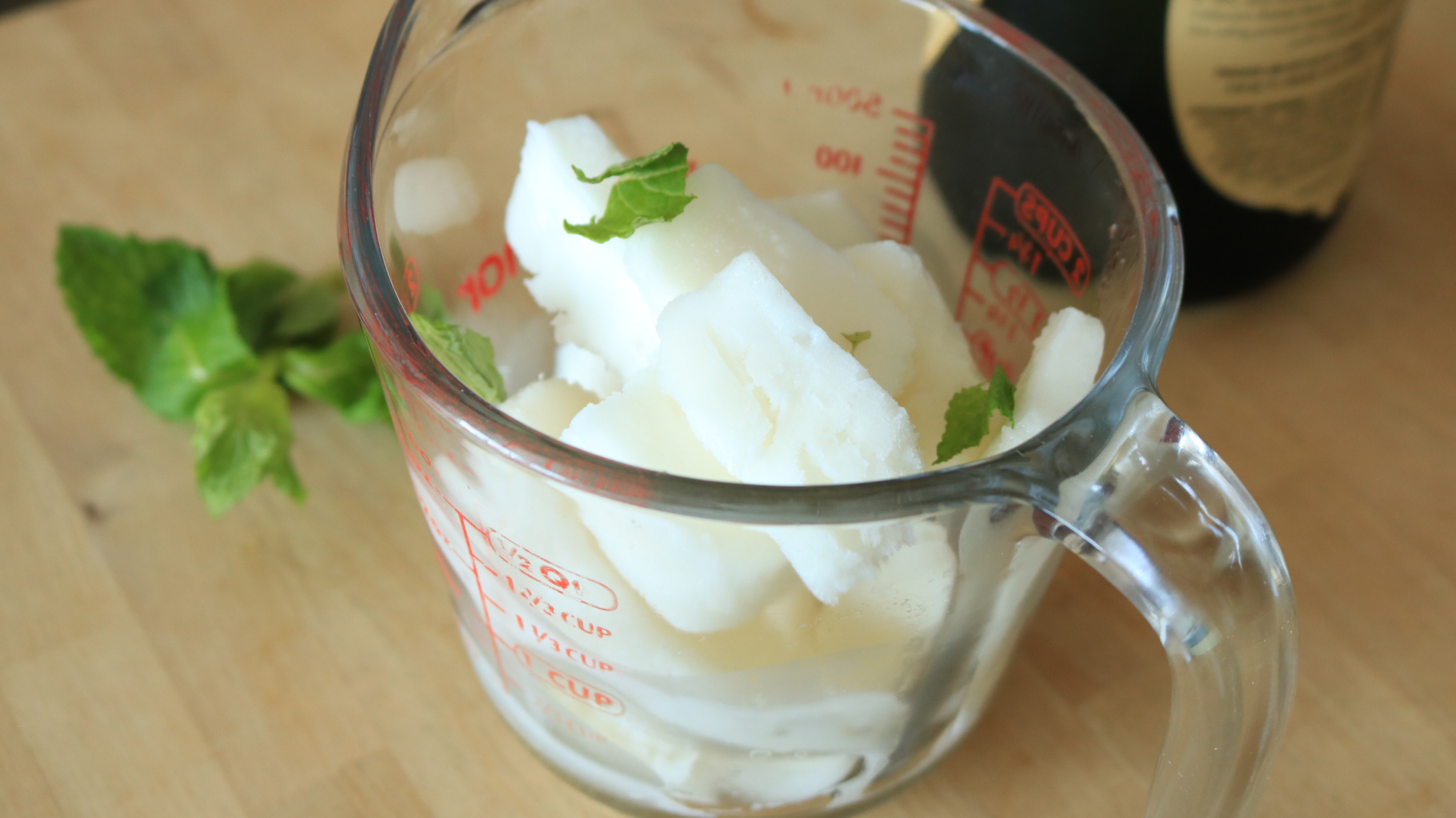 Chopped lemon sorbet in a measuring cup next to mint and a wine bottle.