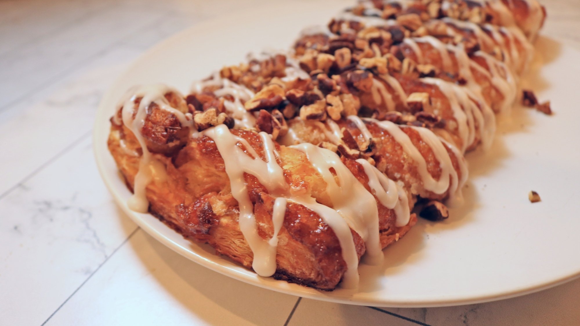 An apple strip pastry with icing and nuts.